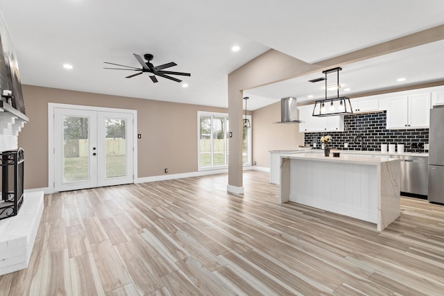 kitchen with decorative light fixtures, white cabinets, wall chimney exhaust hood, lofted ceiling, and a kitchen island with sink