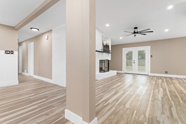 unfurnished living room with a fireplace, french doors, ceiling fan, and light hardwood / wood-style flooring