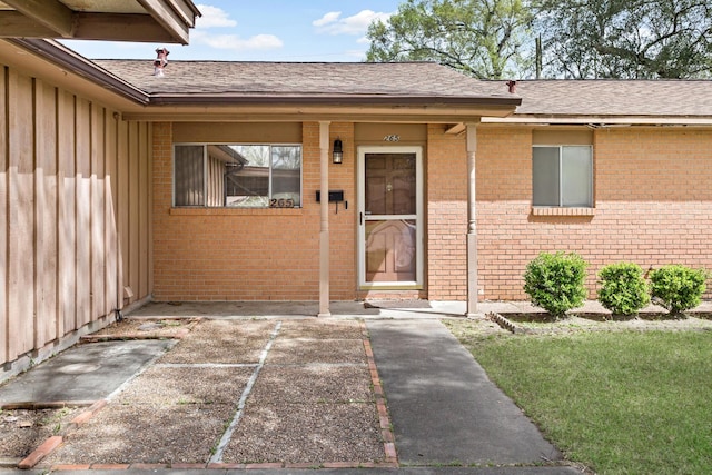 doorway to property featuring brick siding, a shingled roof, and board and batten siding