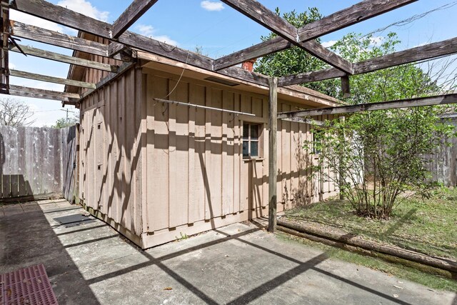 view of outbuilding featuring fence, a pergola, and an outbuilding