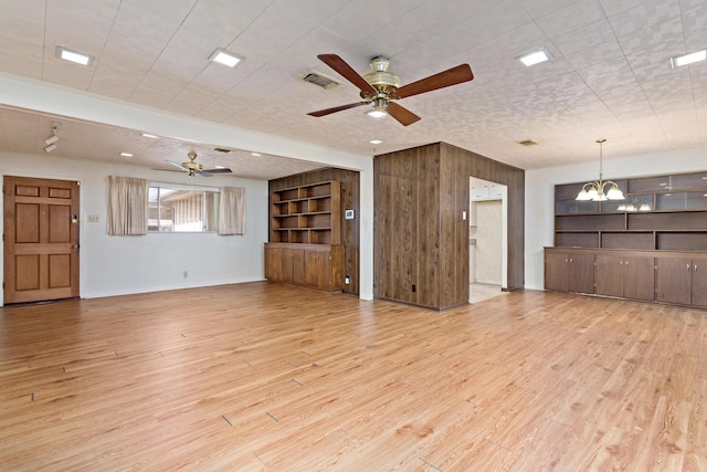 unfurnished living room with a ceiling fan, a chandelier, light wood-type flooring, and wood walls