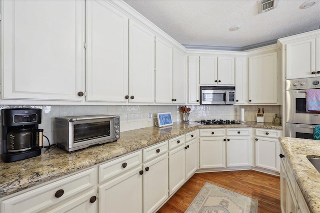 2175 Brewton Cir, Beaumont, TX 77706 - kitchen with stainless steel appliances, white cabinetry, tasteful backsplash, light wood-type flooring, and a textured ceiling