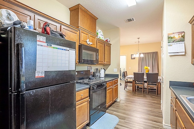 kitchen featuring black appliances, light wood finished floors, brown cabinets, dark countertops, and a textured ceiling