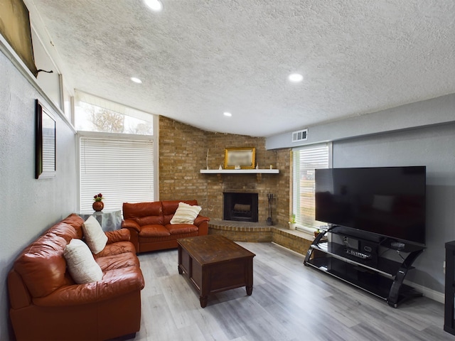 living room with lofted ceiling, a brick fireplace, light hardwood / wood-style flooring, and a textured ceiling