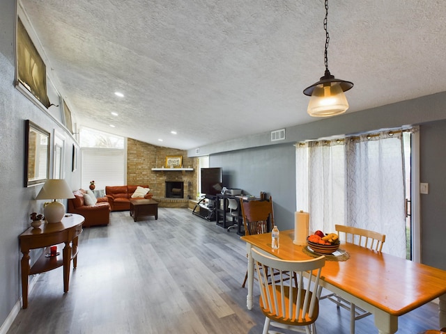 dining room featuring wood-type flooring, vaulted ceiling, a textured ceiling, and a fireplace