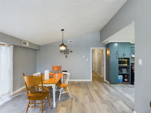 dining space with hardwood / wood-style flooring, vaulted ceiling, and a textured ceiling