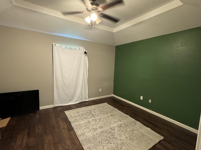 empty room with dark hardwood / wood-style floors, ceiling fan, a raised ceiling, and a textured ceiling