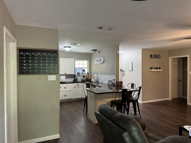 kitchen with kitchen peninsula, sink, dark hardwood / wood-style floors, white cabinetry, and a breakfast bar area