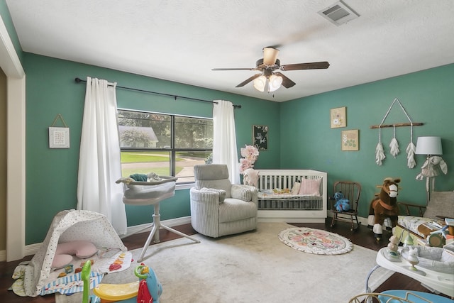 bedroom featuring ceiling fan, a crib, and a textured ceiling