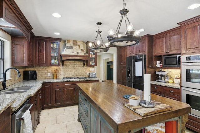 kitchen with premium range hood, stainless steel appliances, sink, an inviting chandelier, and butcher block counters