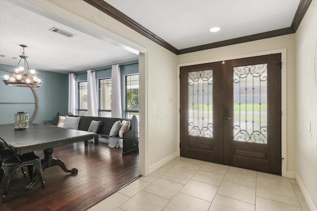 entryway with an inviting chandelier, light tile patterned flooring, crown molding, and french doors