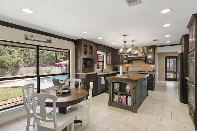 kitchen featuring stainless steel appliances, hanging light fixtures, an island with sink, dark brown cabinets, and custom exhaust hood