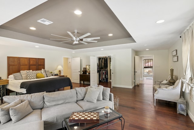 bedroom featuring a walk in closet, a tray ceiling, ceiling fan, dark hardwood / wood-style floors, and a closet