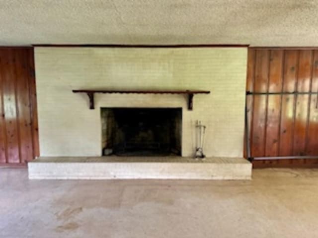 unfurnished living room featuring a brick fireplace, wooden walls, and a textured ceiling