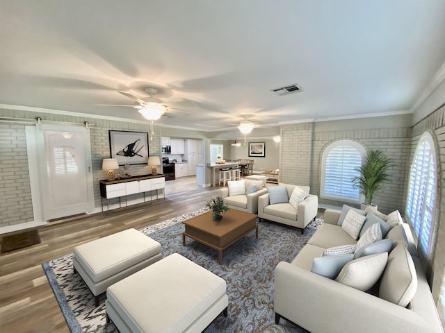 living room with ceiling fan, brick wall, wood finished floors, visible vents, and ornamental molding