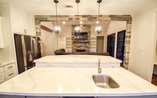 kitchen with light stone countertops, stainless steel refrigerator with ice dispenser, pendant lighting, and an island with sink