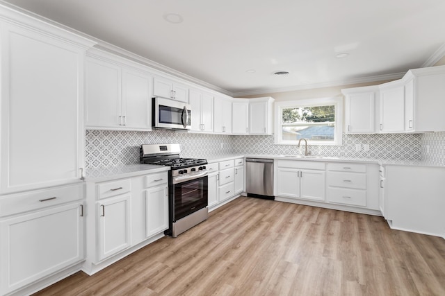 kitchen featuring sink, ornamental molding, light hardwood / wood-style floors, white cabinetry, and stainless steel appliances