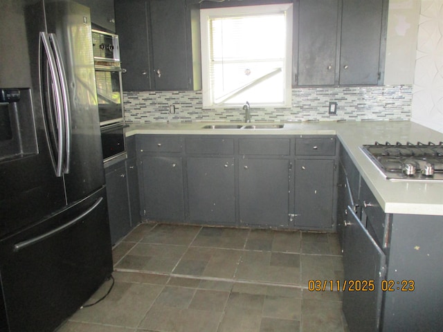 kitchen with a sink, decorative backsplash, gray cabinetry, light countertops, and stainless steel appliances