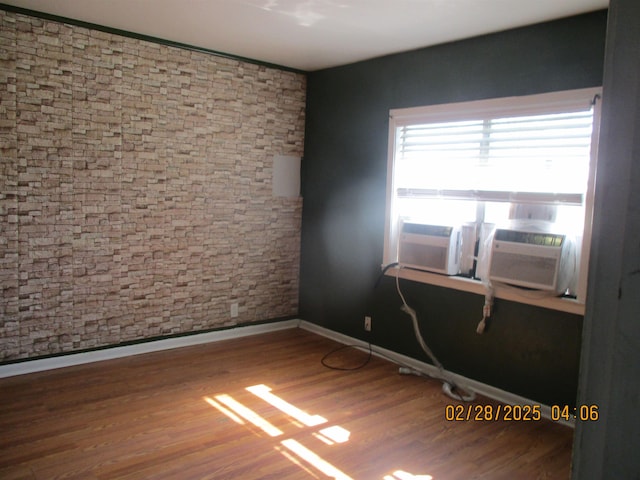 unfurnished room featuring cooling unit, wood finished floors, and baseboards