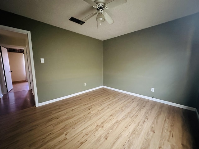 empty room with ceiling fan, a textured ceiling, baseboards, and wood finished floors