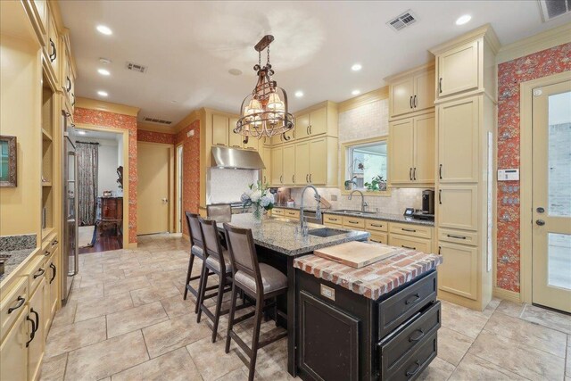 5160 Littlechase Dr, Beaumont, TX 77706 - kitchen featuring under cabinet range hood, cream cabinetry, an island with sink, a sink, and recessed lighting