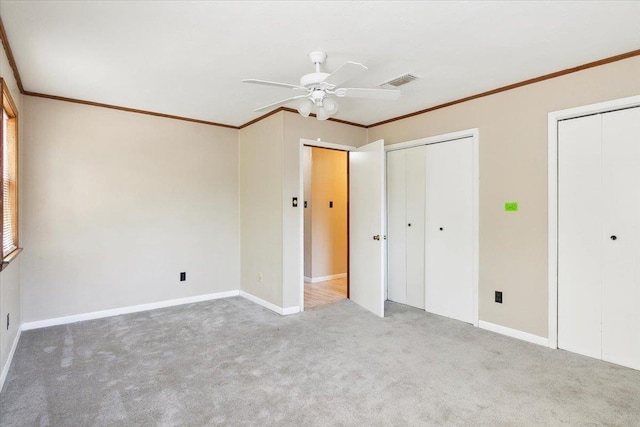 unfurnished bedroom with carpet, multiple closets, ceiling fan, and ornamental molding