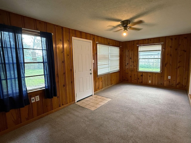 foyer entrance featuring light carpet, a textured ceiling, ceiling fan, and wooden walls