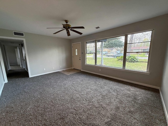 spare room with ceiling fan, plenty of natural light, and dark colored carpet