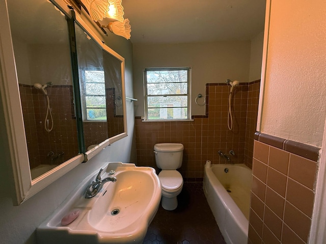 full bathroom featuring sink, tiled shower / bath, tile walls, and toilet