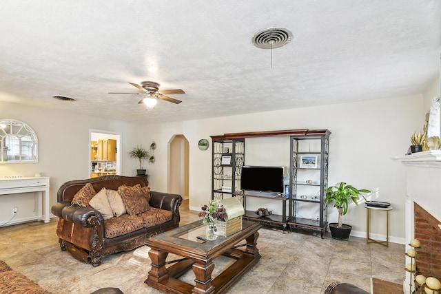 living room featuring ceiling fan, a textured ceiling, and a brick fireplace