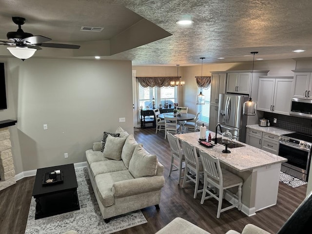 kitchen featuring stainless steel appliances, light stone counters, an island with sink, pendant lighting, and a kitchen bar