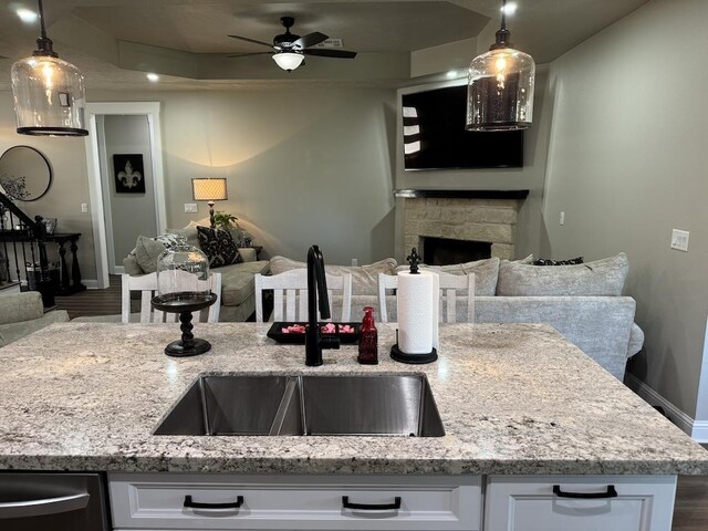 kitchen with white cabinets, sink, hanging light fixtures, ceiling fan, and light stone countertops