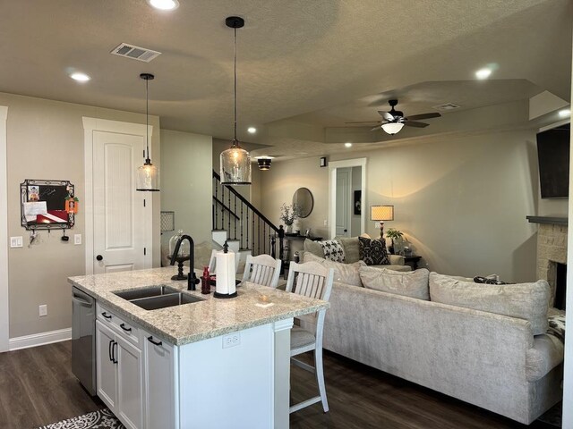 kitchen featuring light stone countertops, a breakfast bar, a kitchen island with sink, decorative light fixtures, and white cabinets