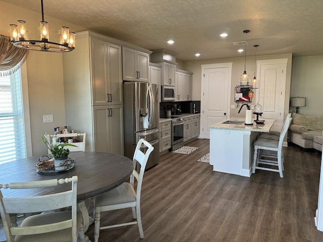 kitchen with hanging light fixtures, light stone counters, an island with sink, gray cabinets, and appliances with stainless steel finishes