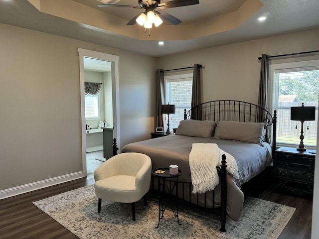 bedroom with multiple windows, dark hardwood / wood-style flooring, a tray ceiling, and ceiling fan