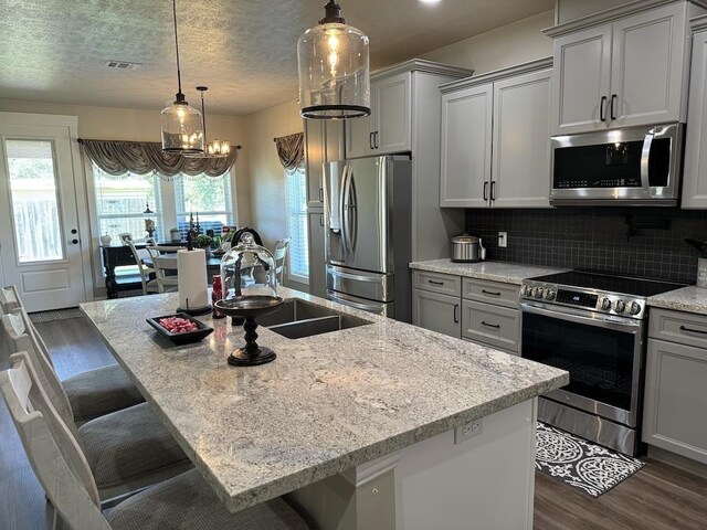 kitchen featuring light stone countertops, sink, a kitchen bar, a kitchen island with sink, and appliances with stainless steel finishes