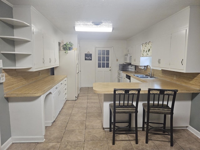 kitchen with kitchen peninsula, a kitchen bar, white appliances, sink, and white cabinets