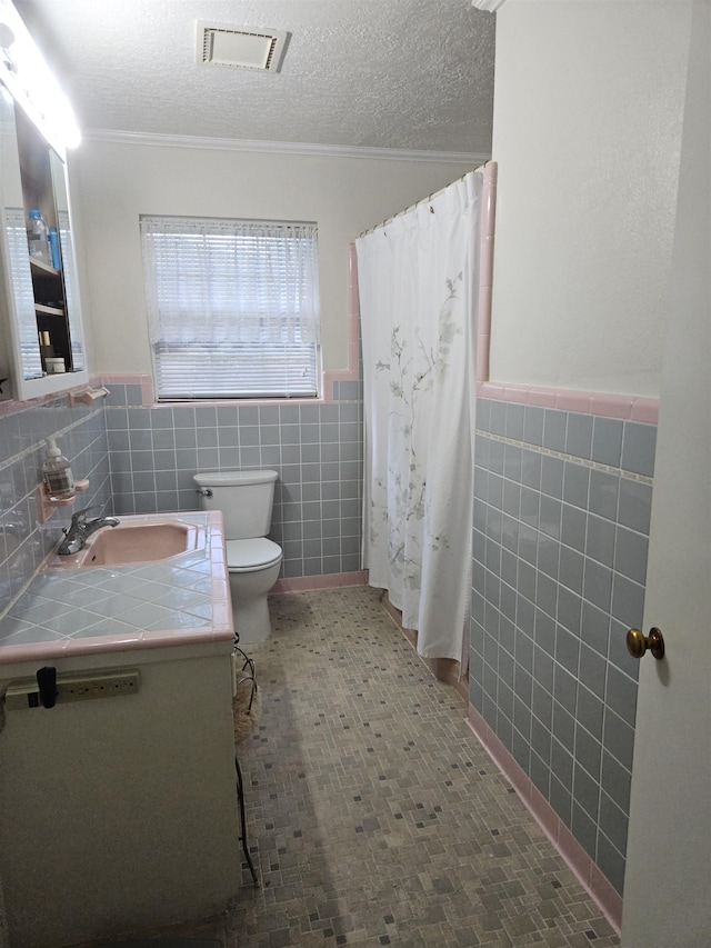 bathroom featuring a textured ceiling, vanity, tile walls, and toilet