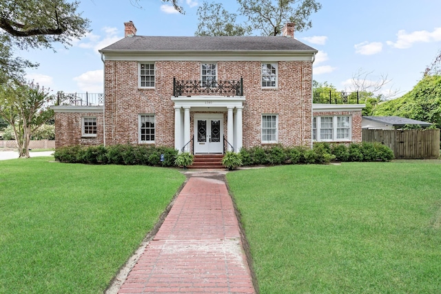 colonial inspired home featuring a balcony, a front yard, and french doors