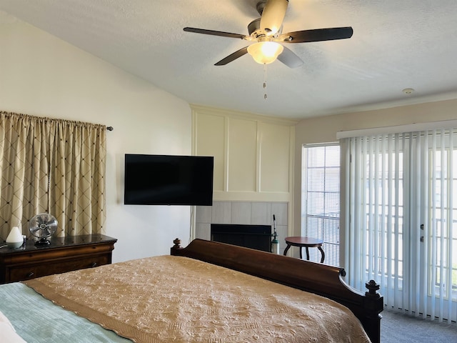 carpeted bedroom featuring ceiling fan, a tile fireplace, a textured ceiling, and access to outside