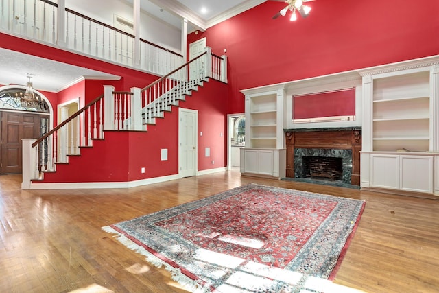 unfurnished living room with a high end fireplace, a towering ceiling, ornamental molding, built in features, and hardwood / wood-style floors