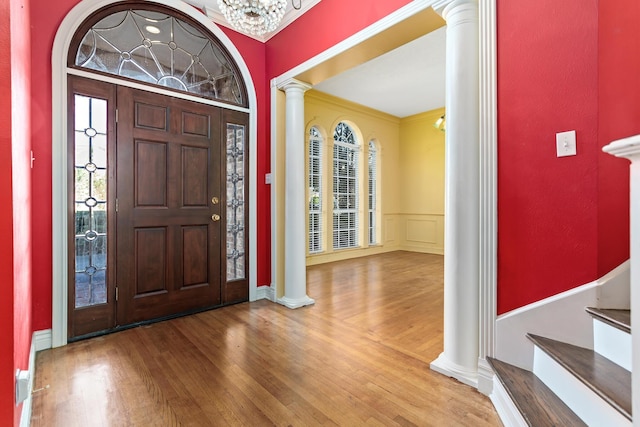 entrance foyer with decorative columns, ornamental molding, wood-type flooring, and a notable chandelier