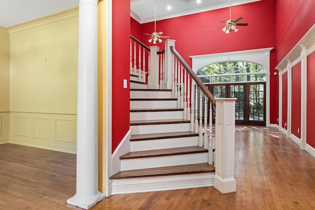 staircase with french doors, crown molding, hardwood / wood-style flooring, ceiling fan, and decorative columns