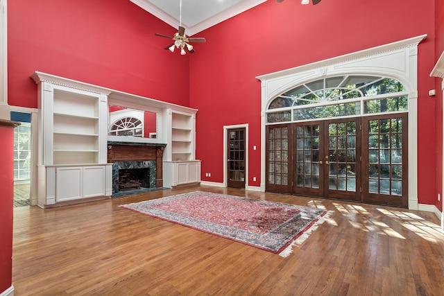 unfurnished living room featuring a high end fireplace, french doors, ceiling fan, hardwood / wood-style flooring, and a high ceiling