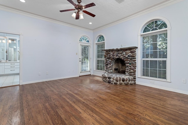 unfurnished living room featuring hardwood / wood-style flooring, ceiling fan, a stone fireplace, and crown molding