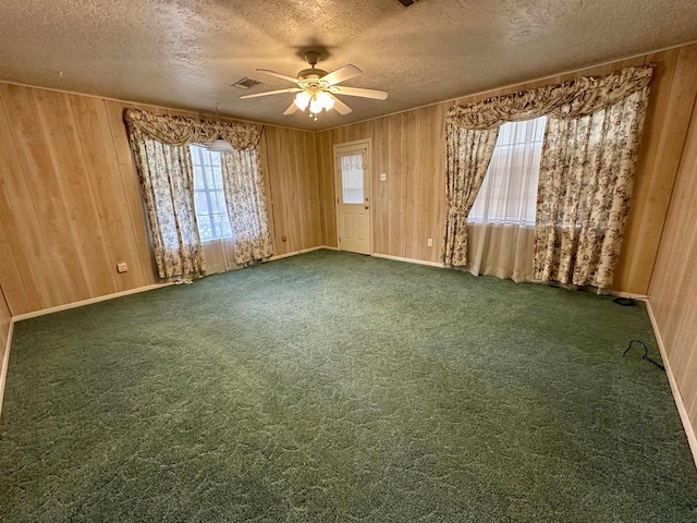 carpeted empty room with ceiling fan, wooden walls, and a textured ceiling