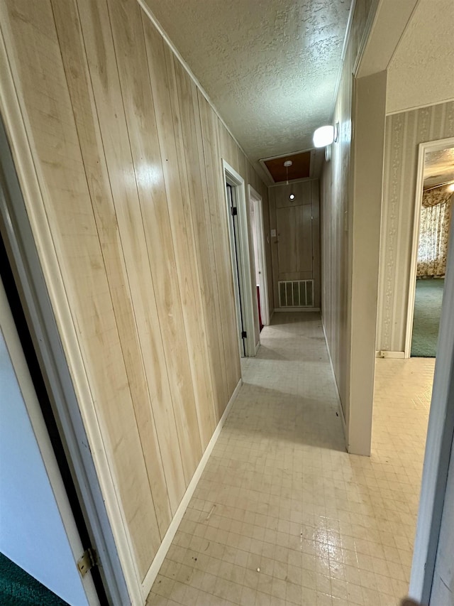 hall with visible vents, wood walls, a textured ceiling, and attic access