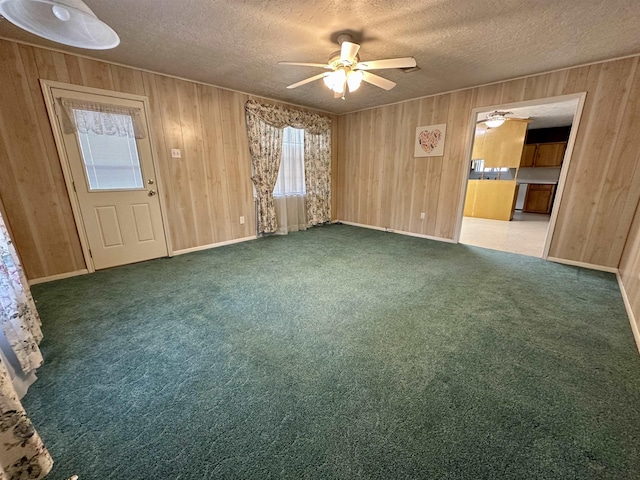 empty room with a textured ceiling, carpet floors, wood walls, and a ceiling fan