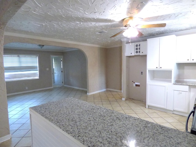 kitchen featuring crown molding, white cabinets, light stone countertops, and light tile patterned floors