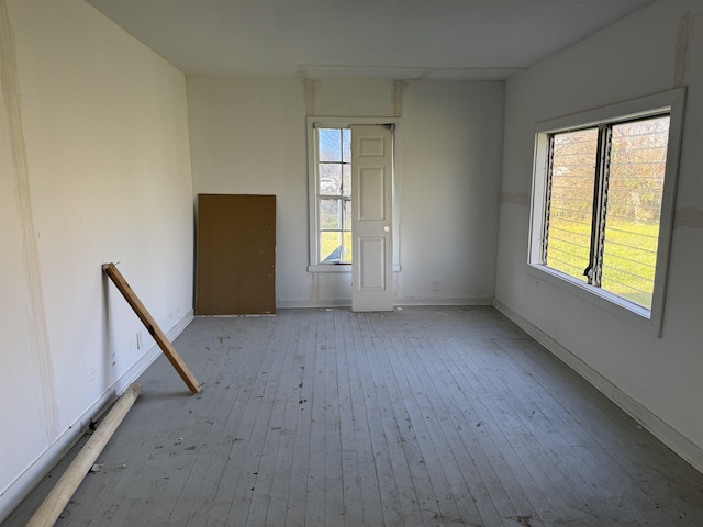 spare room featuring baseboards, wood-type flooring, and a healthy amount of sunlight